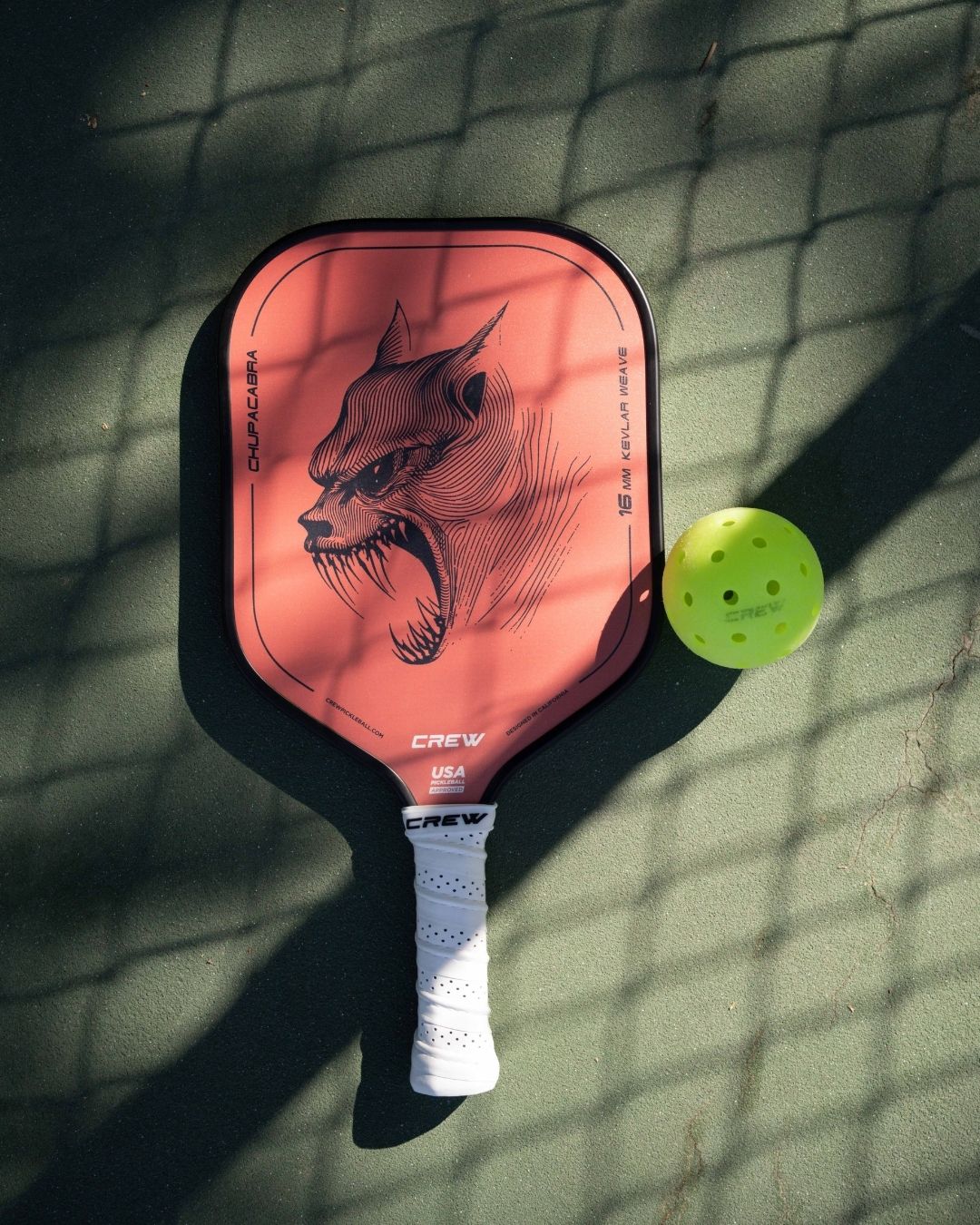Chupacabra pickleball paddle by Crew Pickleball with 16mm kevlar weave core, shown beside a neon yellow ball on a sunlit court, designed for precision control and fierce performance.